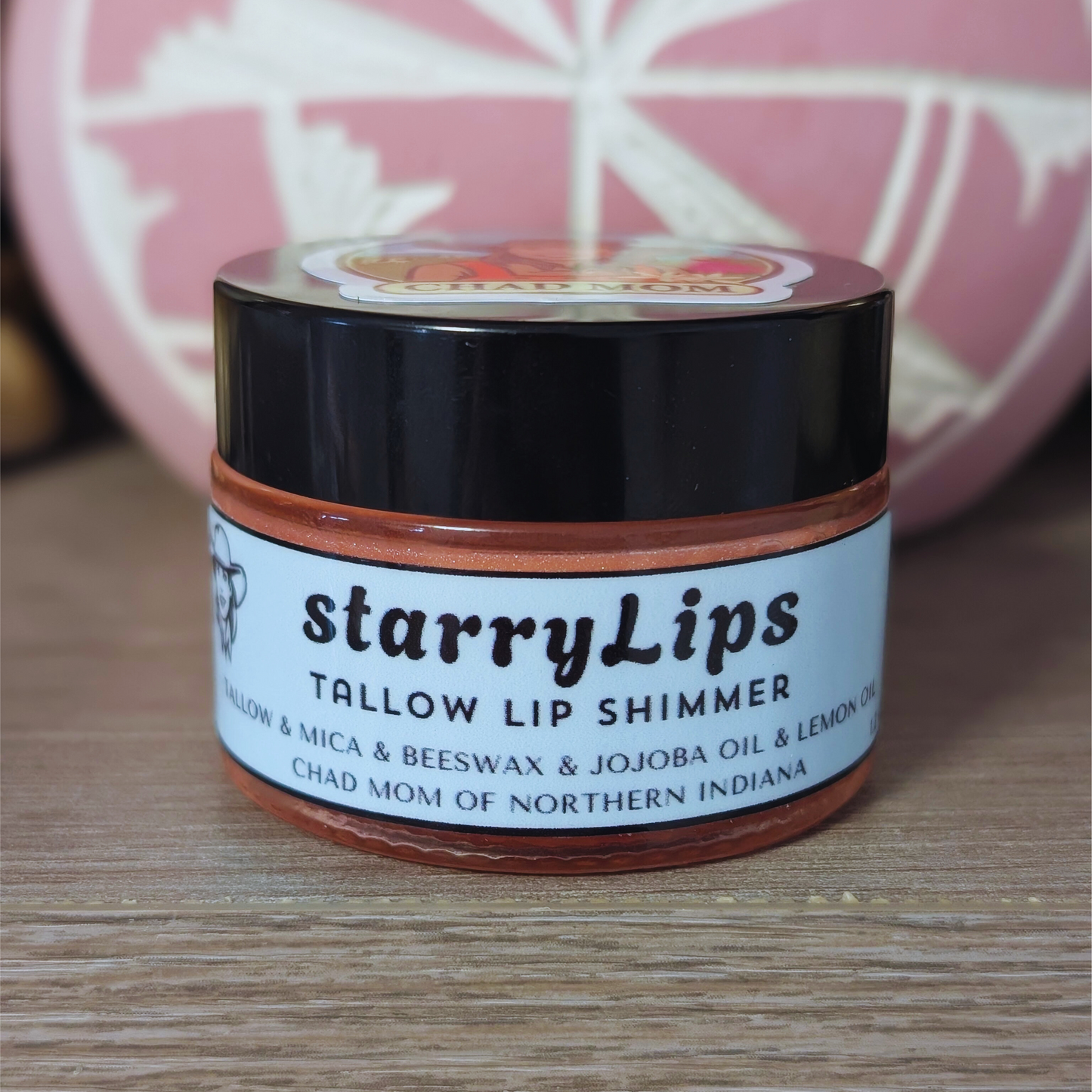 Jar of starryLips tallow lip shimmer on a wooden surface with a blurred background