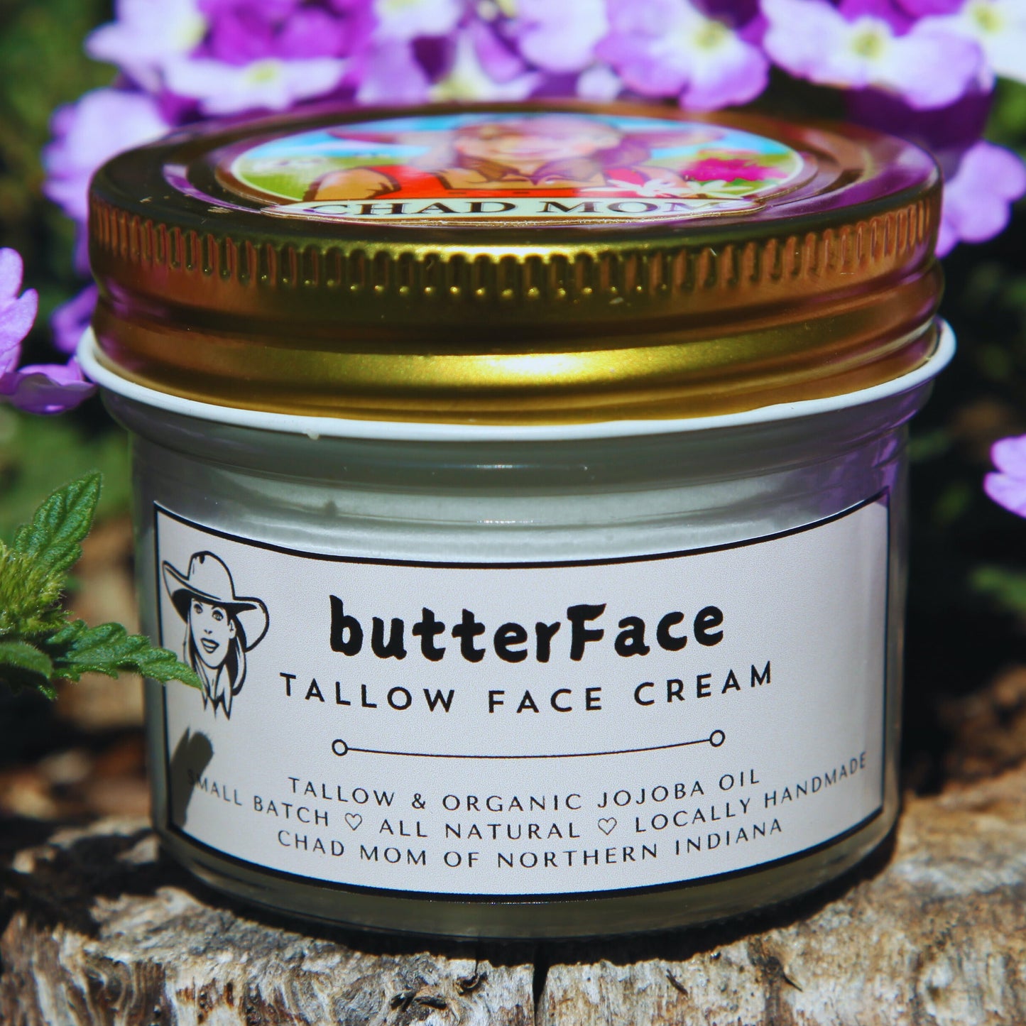 Jar of butterFace tallow face cream on a wooden log with purple flowers in the background